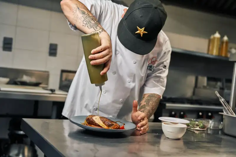 A chef carefully plating a dish with foraged herbs and flowers