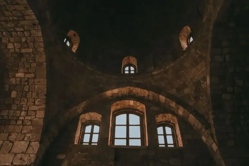 Interior of Abuna Yemata Guh rock-hewn church, showing ancient frescoes and a priest, view from inside towards the difficult entrance, Tigray, Ethiopia, dramatic shafts of light illuminating painted ceiling